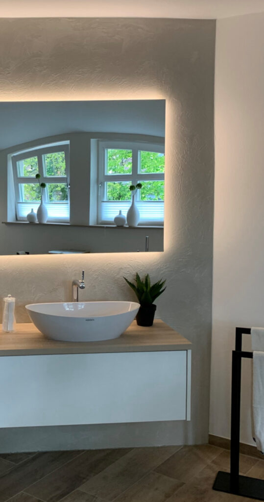 Waschtisch mit ovalem Waschbecken, beleuchtetem Spiegel und Holzoberfläche für ein hochwertiges Badezimmerambiente